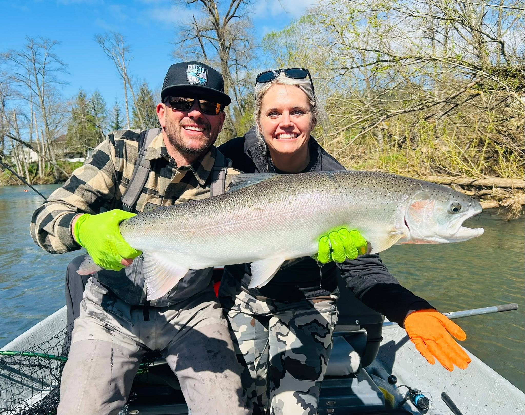 Two anglers smiling behind a large winter steelhead on a sunny Oregon river