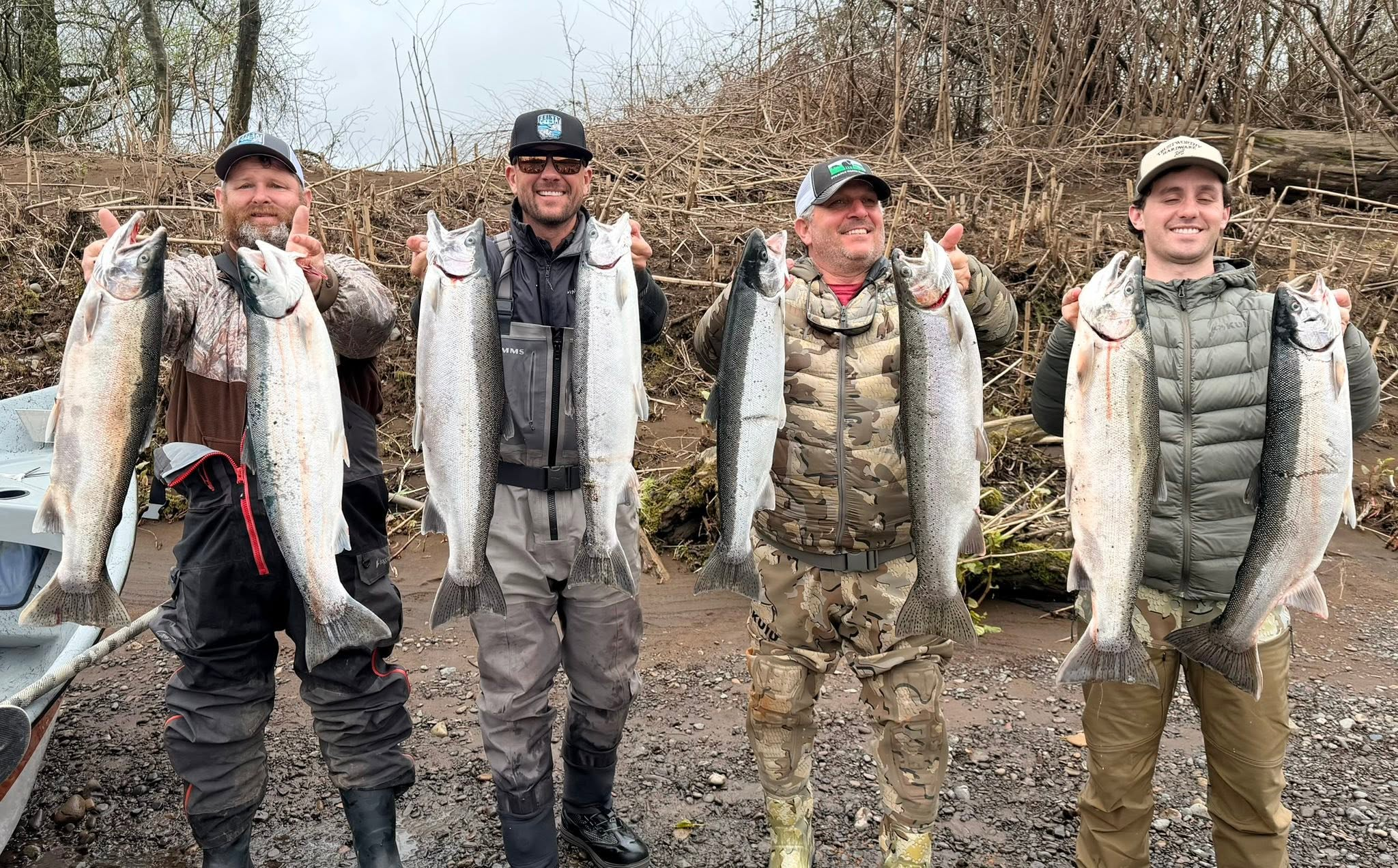 Four winter steelhead anglers displaying their catch on the riverbank